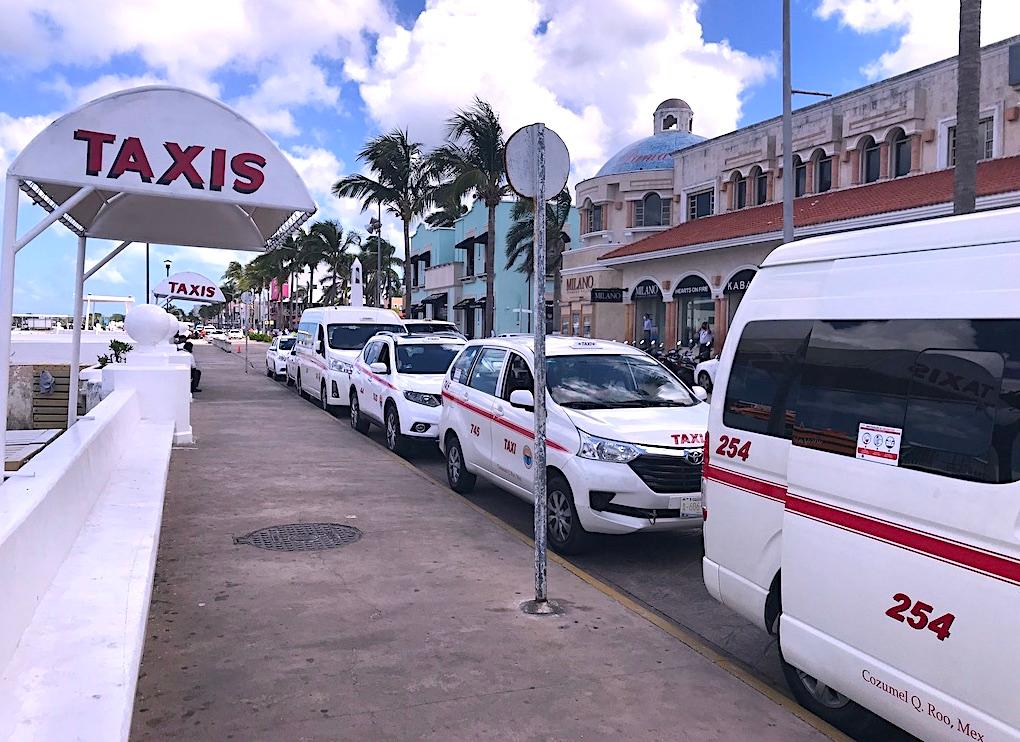 Line of numbered white and red taxis waiting at the rank on the Melgar waterfront in San Miguel de Cozumel, under a TAXIS sign